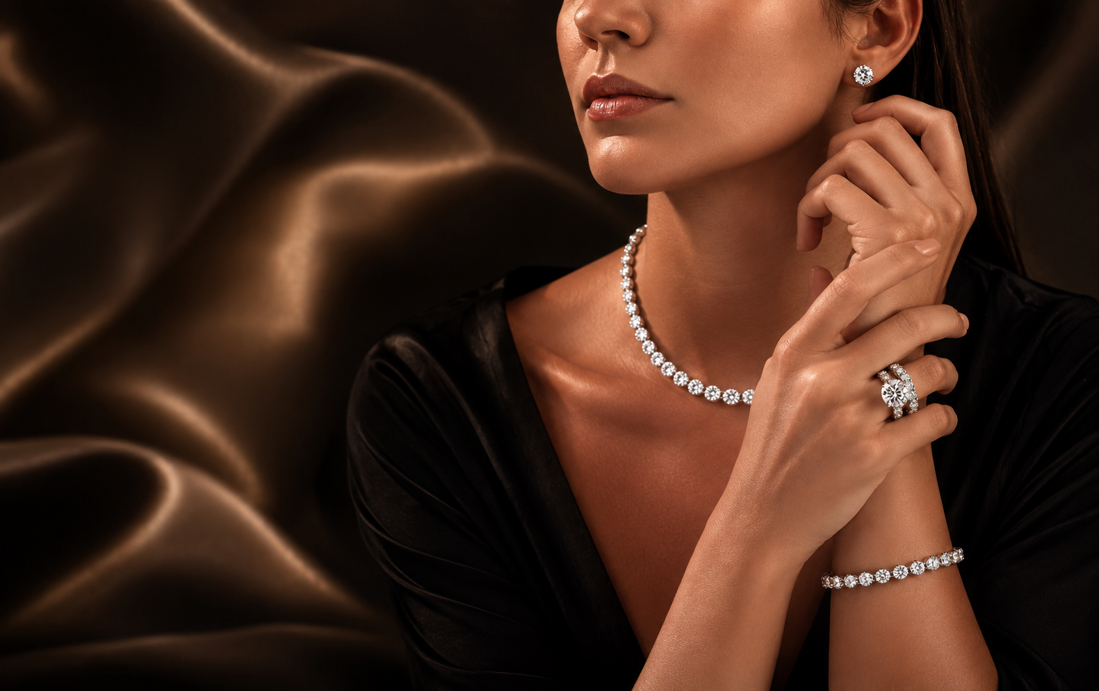 A woman wearing a sparkling diamond necklace, matching stud earring, ring, and bracelet, posed against a dark brown draped satin background.